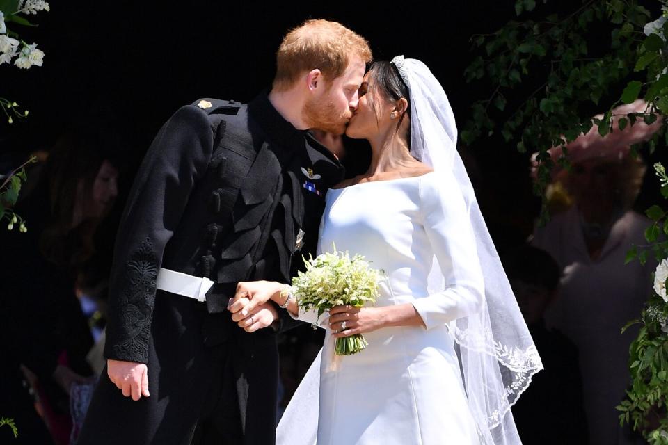 Prince Harry, Duke of Sussex kisses his wife Meghan, Duchess of Sussex as they leave from the West Door of St George's Chapel