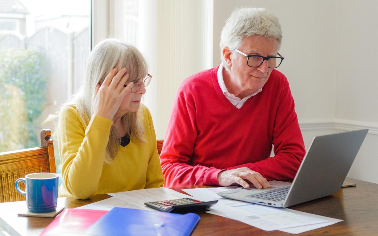 A senior couple check their finances at home while surrounded by documents, folders, laptop and a calculator