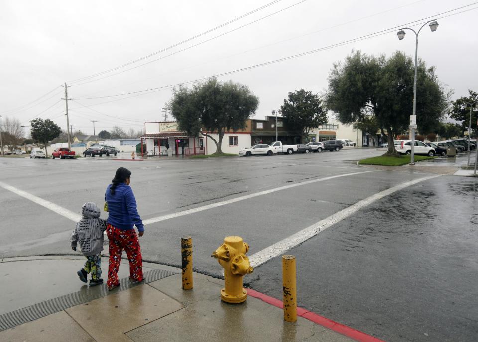 A woman and child cross an intersection on Wednesday, Feb. 26, 2014, in King City, Calif. The acting police chief and two officers in King City were removed from duty after being arrested on suspicion of selling or giving away the impounded cars of poor residents, authorities said. (AP Photo/Marcio Jose Sanchez)