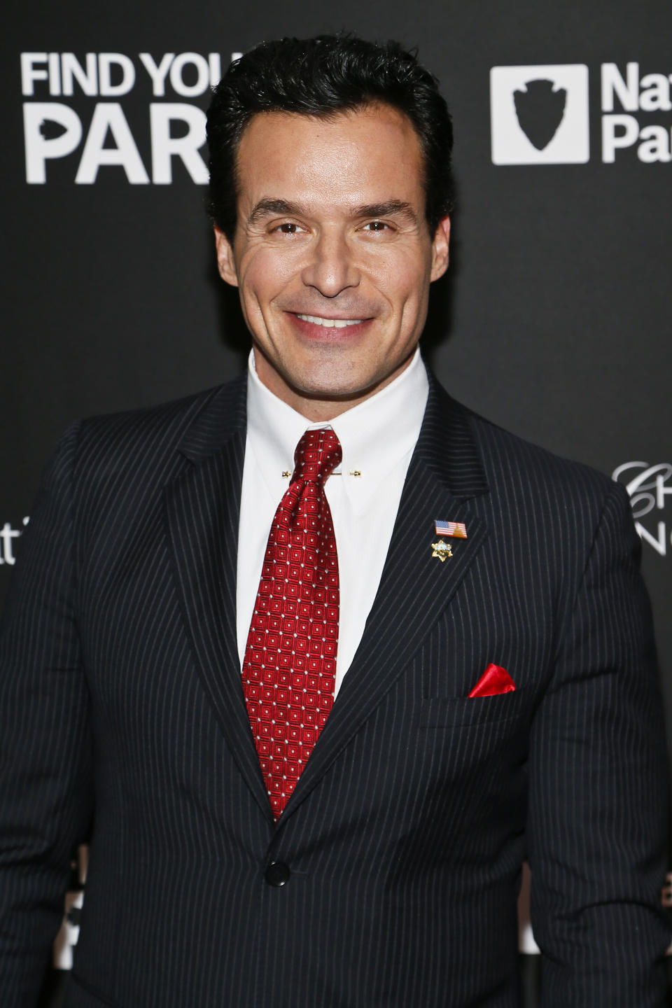Man in pinstripe suit with patterned red tie and lapel pin smiles at a National Parks event
