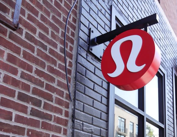 Sign with lululemon logo hanging from post sticking out of a brick wall.