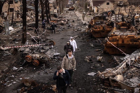 BUCHA, UKRAINE - APRIL 06: People walk through debris and destroyed Russian military vehicles on a street on April 06, 2022 in Bucha, Ukraine. The Ukrainian government has accused Russian forces of committing a 