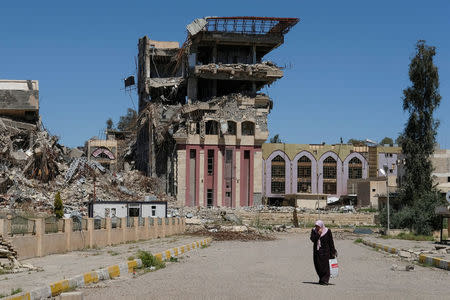 A woman walks in front of the remains of the University of Mosul. REUTERS/Marko Djurica