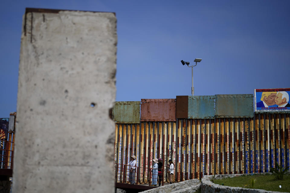 People walk along the wall that separates the United States from Mexico, near a slab of the Berlin Wall, in Tijuana, Mexico, Friday, Aug. 25, 2023. The 3-ton pockmarked, gray concrete slab sits between a bullring, a lighthouse and the border wall, which extends into the Pacific Ocean. (AP Photo/Gregory Bull) (AP Photo/Gregory Bull)