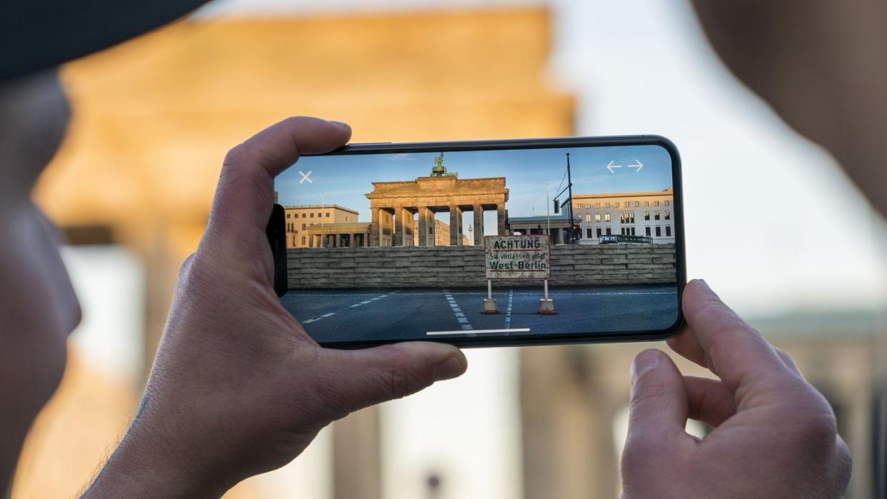 Apple-Chef Tim Cook lässt sich am Brandenburger Tor von Entwickler Peter Kolski das Projekt «MauAR» auf einem Smartphone erklären. Foto: Brooks Kraft/Apple