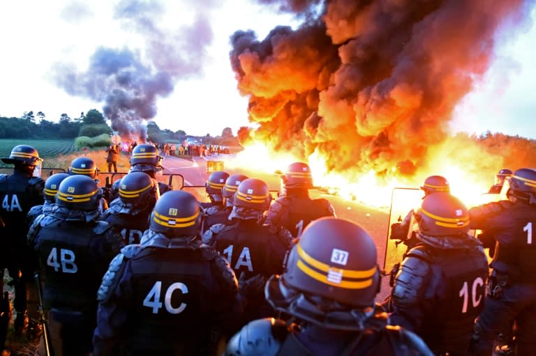 Riot police stand guard behind a fire as refinery workers hold a blockade of the oil depot of Douchy-Les-Mines to protest against the government's proposed labour reforms, on May 25, 2016