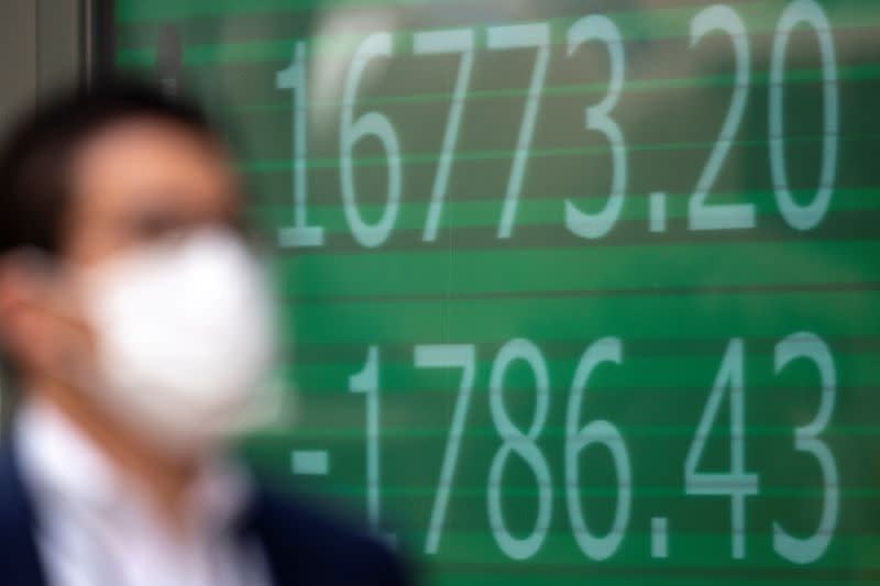 A man wearing a protective face mask walks past a screen showing Nikkei index outside a brokerage in Tokyo