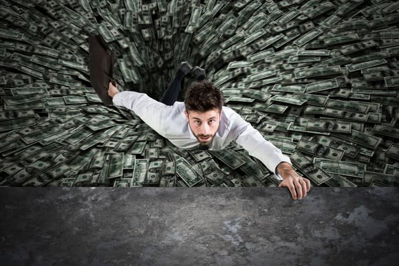 Businessman being pulled into a black hole of money.