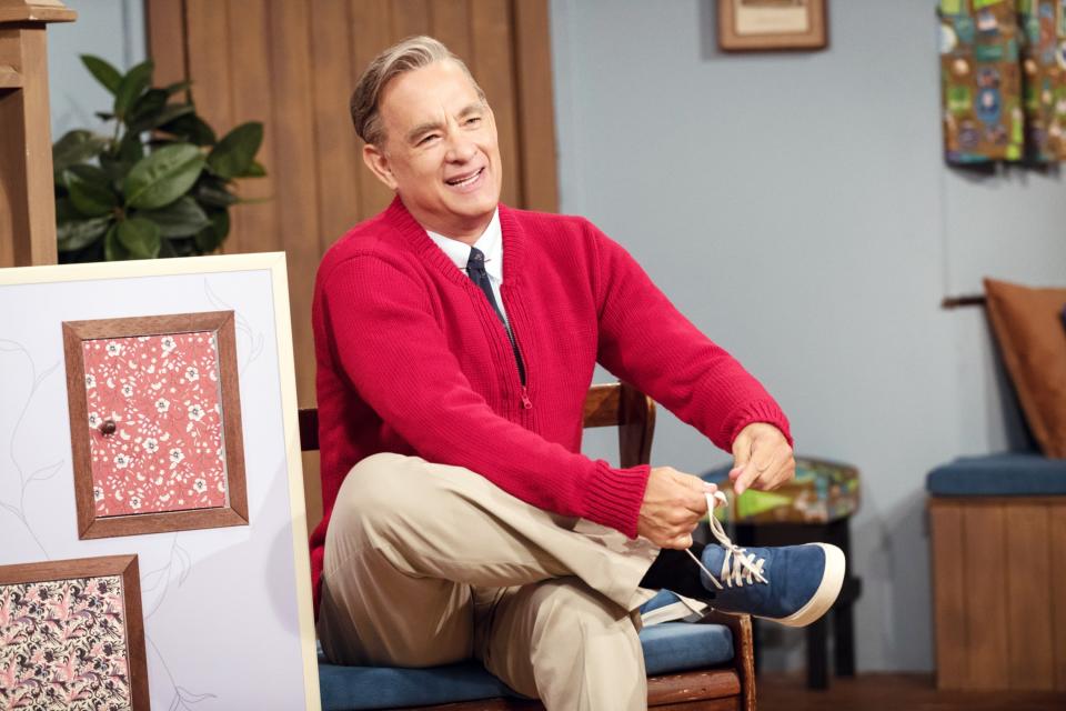 Fred Rogers dressed in sneakers, pants, a shirt and tie, and a sweater