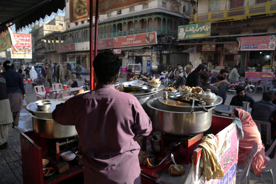 People eat breakfast at a famus food street of Gawalmandi, an old area of Lahore, Pakistan, Sunday, Dec. 11, 2022. Gawalmandi is the city's neighborhood crammed with people, vehicles, animals, and food stalls. (AP Photo/K. M. Chaudary)