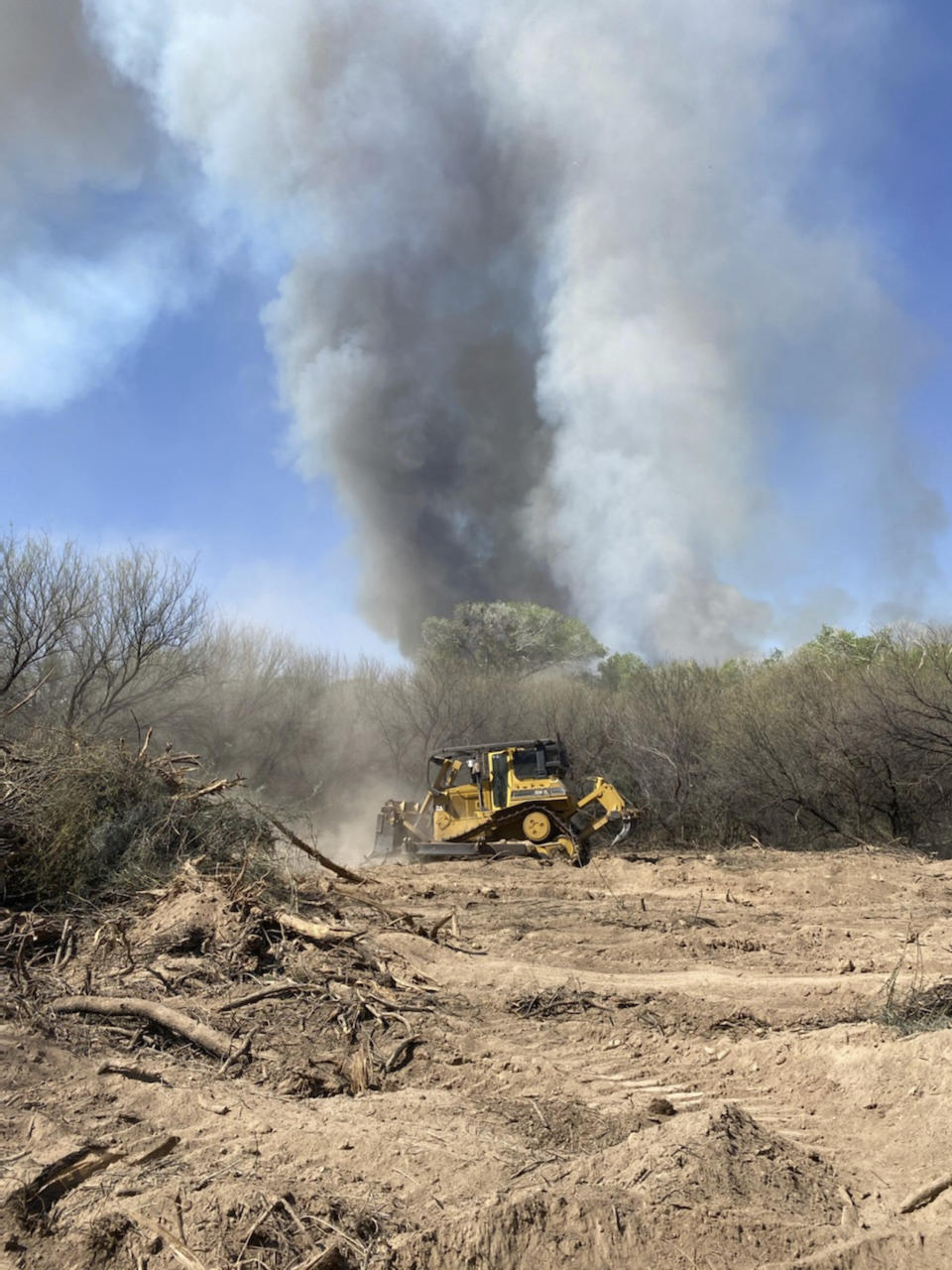 In this Friday, April 9, 2021, photo provided by the Arizona Department of Forestry and Fire Management, Heavy machinery clear thick tamarisk in a river bottom as the Pinal County Wildfire burns near rural properties in Dudleyville, Ariz. A small community in south-central Arizona remained under an evacuation notice Friday after crews and air tankers stopped the growth of a wildfire that burned at least 12 homes, officials said. (Arizona Department of Forestry & Fire Management via AP)