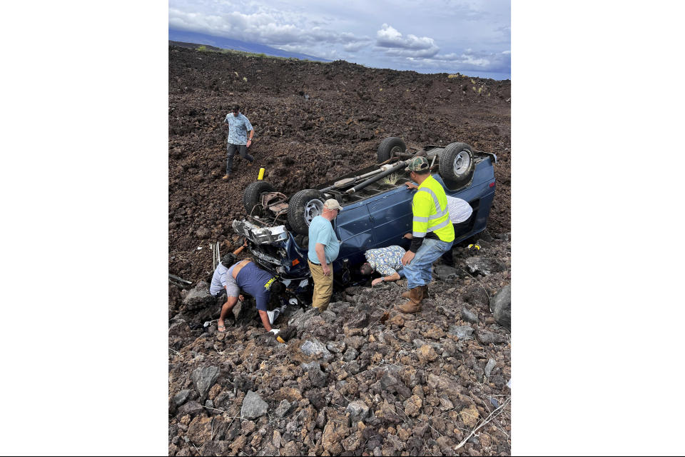 Hawaii Gov. Josh Green, middle, kneels down to look under an upside down vehicle's driver at the scene of an accident in Waikoloa, Hawaii on Thursday, May 18, 2023. Gov. Green, who has worked as an emergency room doctor in rural parts of the Big Island stopped to help out when his security detail spotted a vehicle upside down in a lava field Thursday while en route to a Big Island event. The man suffered a few cuts and bruises and seemed to be OK, Green said. (Reece Kainoa Kilbey/Office of the Governor, State of Hawai'i via AP)