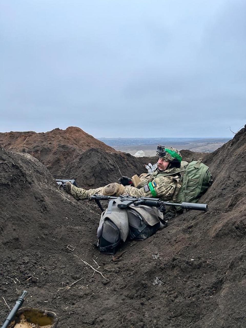 Yabchanka in combat gear sits amid piles of soil outside Bakhmmut