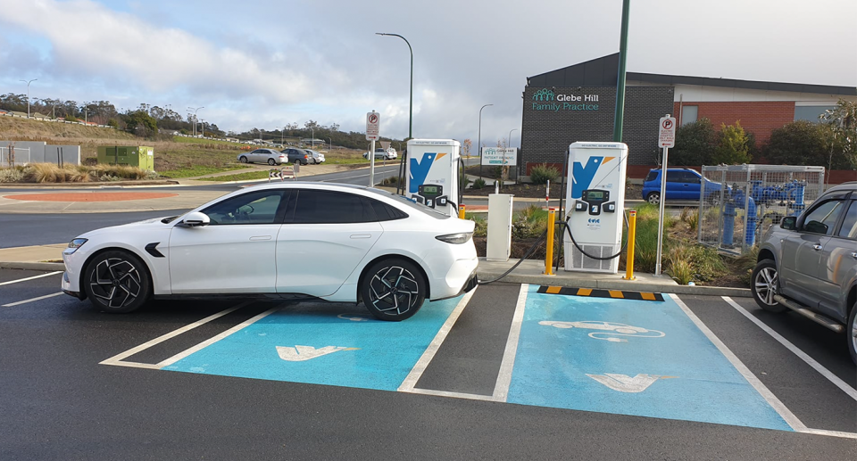 An electric vehicle motorist is seen parked using a charger at one station, parking over another, and two separate motorcycle bays.