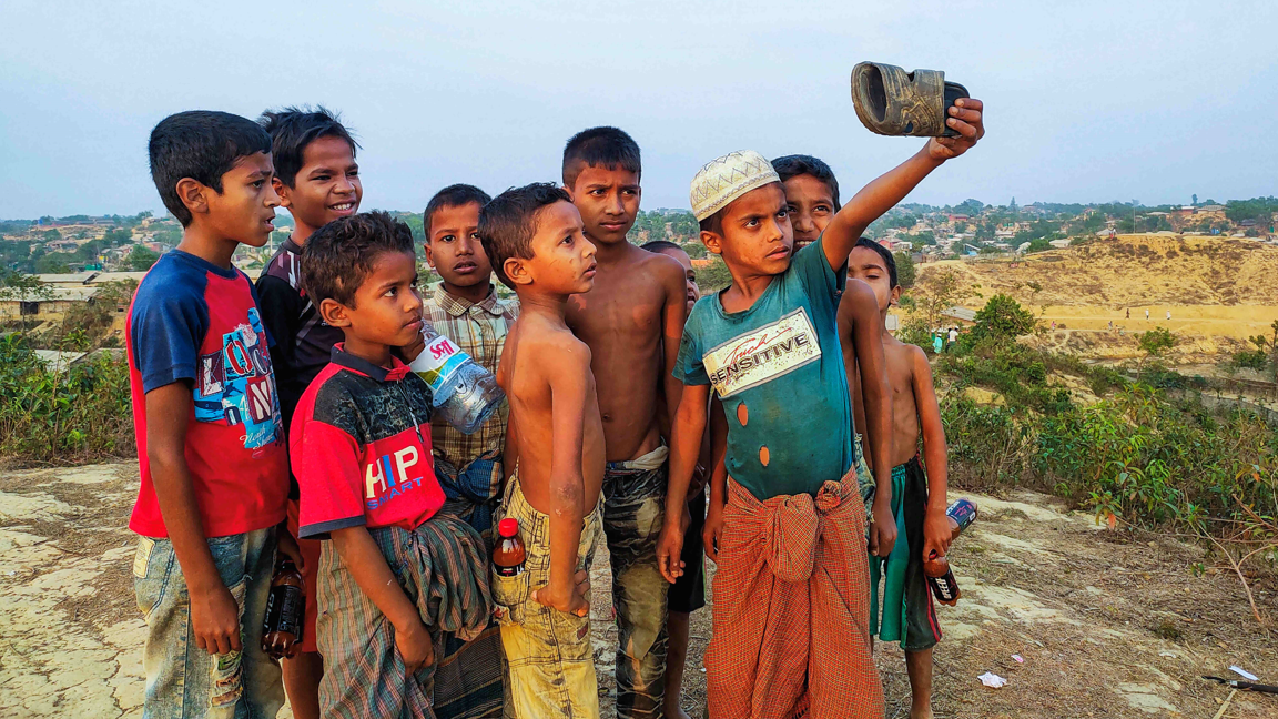 Children pretending to take a selfie at a refugee camp by using a sandal as a phone
