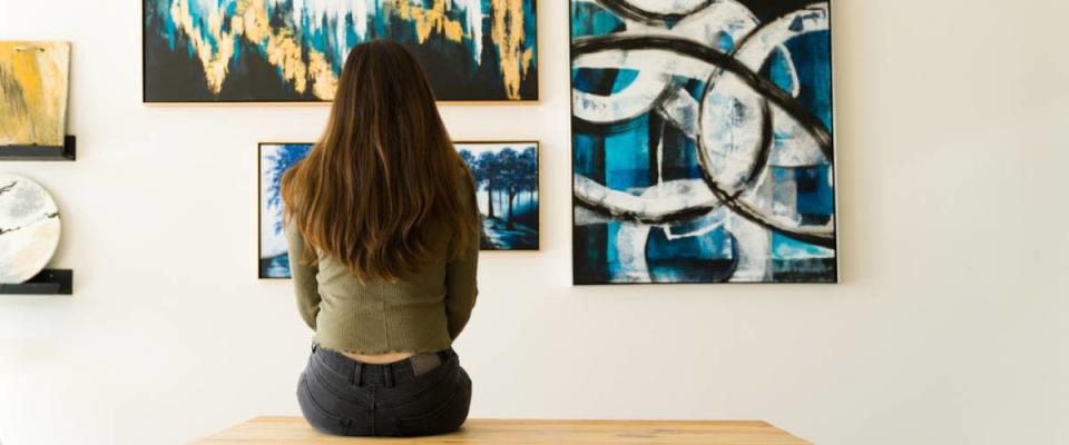 Young female visitor looking reflective while sitting on a bench and admiring the various paintings on the wall of an art gallery