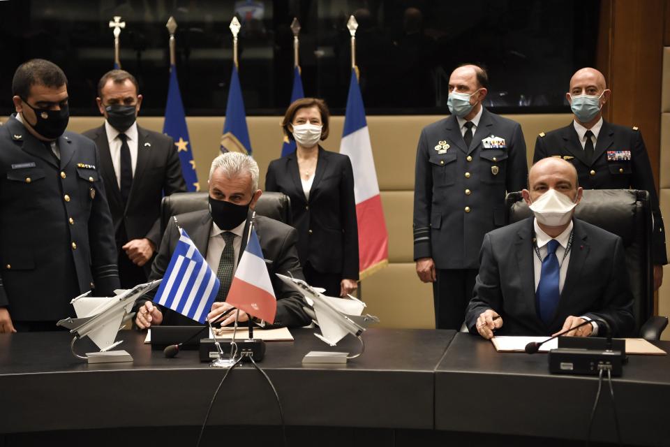 Officials sign the Rafale warplane deal as French Defense Minister Florence Parly, background second left, and her Greek counterpart Nikos Panagiotopoulos, background left, attend the ceremony in Athens, Monday, Jan. 25, 2021. Greece is due to sign a 2.3 billion euro ($2.8 billion) deal with France Monday to purchase 18 Rafale fighter jets to address tension with neighbor Turkey. (Louisa Gouliamaki/Pool via AP)