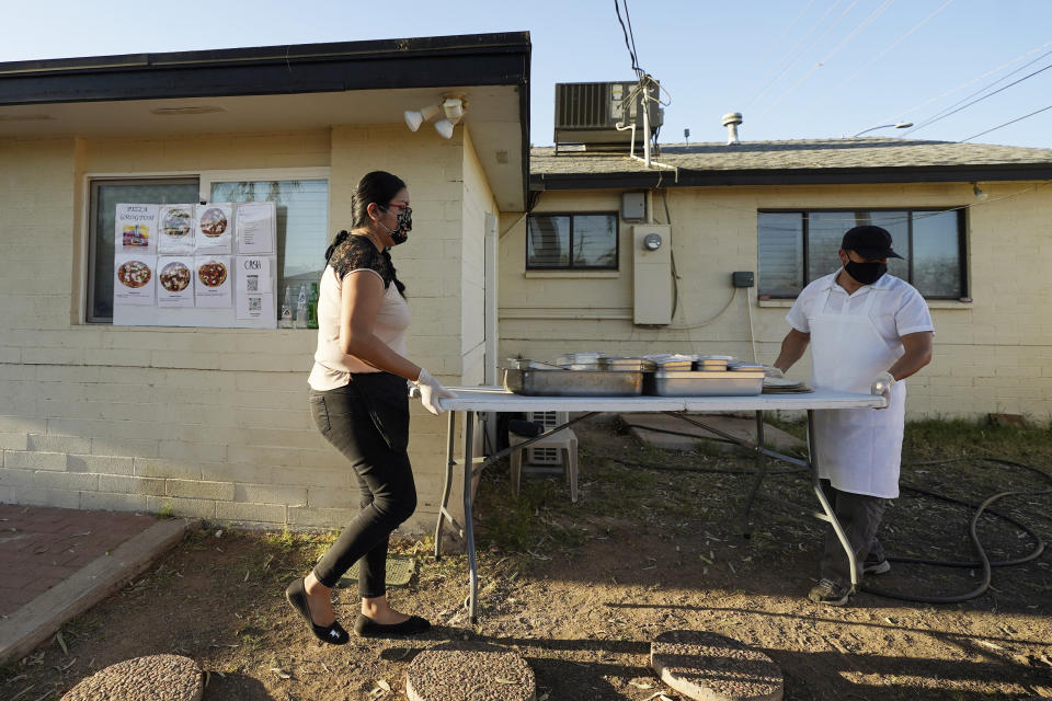 Ruby Salgado, left, and chef Jose Hernandez set up their pizza making station in the backyard of their home in Scottsdale, Ariz. on April 3, 2021. Beaten down by the pandemic, some laid-off or idle restaurant workers have pivoted to dishing out food from home. (AP Photo/Ross D. Franklin)