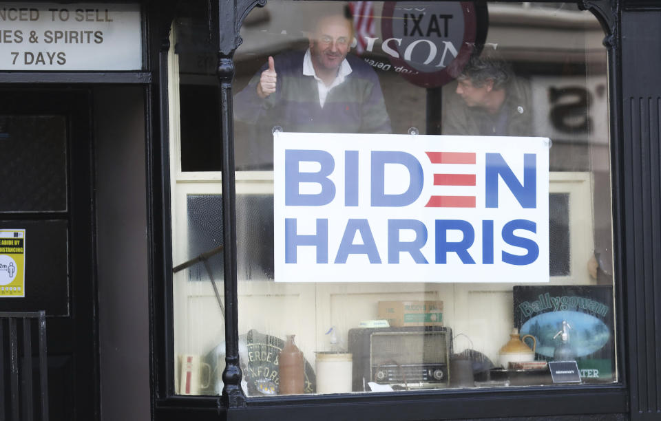 Derek Leonard gestures, behind a poster supporting Joe Biden in the town of Ballina, Ireland, Saturday, Nov. 7, 2020. Biden was elected Saturday as the 46th president of the United States, defeating President Donald Trump in an election that played out against the backdrop of a pandemic, its economic fallout and a national reckoning on racism. (AP Photo/Peter Morrison)