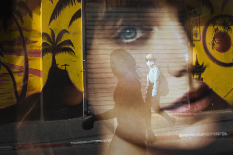 A woman is reflected on a bus station as she wears a protective face mask amid concerns over the country's coronavirus outbreak, in Tel Aviv, Israel, Monday, April 6, 2020. (AP Photo/Oded Balilty)