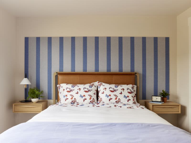 Small bedroom with floating wood nightstands, a bed with butterfly sheets, and a leather headboard in front of a decorative installation of Felt Right felt tiles laid in a blue and gray pinstripe pattern to help reduce noise and echo.