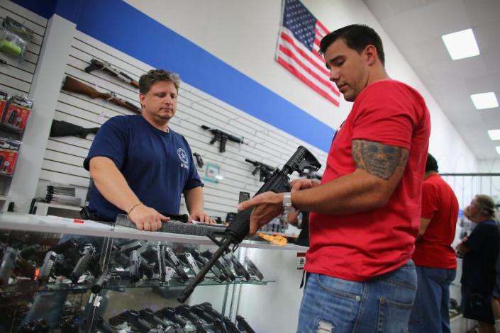 مردی در مغازه اسلحه فروشی به تفنگ نگاه می کند