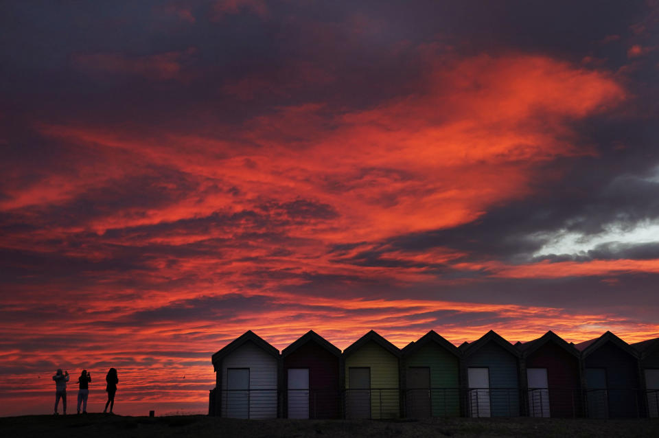 People take photos by colourful beach huts, in front of the red sky at sunrise in Blyth, Northumberland, England, Tuesday, Feb. 23, 2021. (Owen Humphreys/ PA via AP)