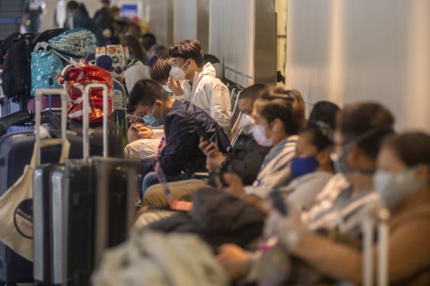 LOS ANGELES, CA - APRIL 02: Wearing a tyvek suit, Ryan Wang, 21, middle, is sitting in a crowded seating area as he waits for a flight at LAX on Friday, April 2, 2021 in Los Angeles, CA. The US Centers for Disease Control and Prevention on Friday released a highly anticipated update to travel guidance for people who are fully vaccinated against Covid-19, eliminating some testing and quarantine recommendations. The CDC says that fully vaccinated people can travel at low risk to themselves. However, the CDC recommends people should still not travel. (Francine Orr/ Los Angeles Times)