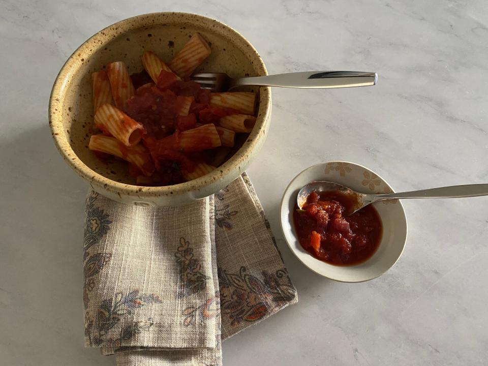 Bowl of pasta with marinara sauce next to a small bowl of a dark-red marinara sauce