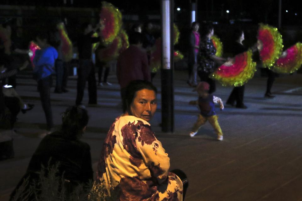 In this Sept. 20, 2018, photo, an Uighur woman looks back as Han Chinese dance in front of restaurants and shophouses operated by Uighur people at the Unity New Village in Hotan, in western China's Xinjiang region. While thousands of Uighur Muslims across China’s Xinjiang region are forced into re-education camps, China’s fledgling vision for ethnic unity is taking shape in a village where Han Chinese work and live alongside Uighur minorities. (AP Photo/Andy Wong)