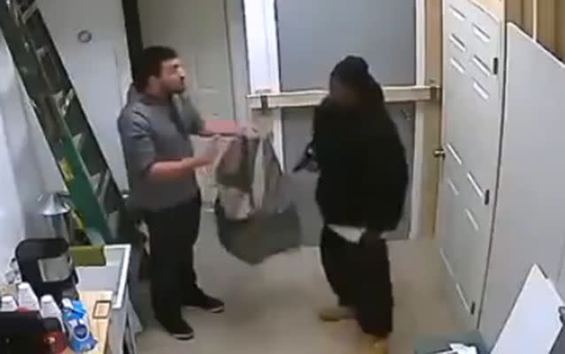 The armed robber gives the man a grey bag to put phones, cash and other products in. Source: LiveLeak.