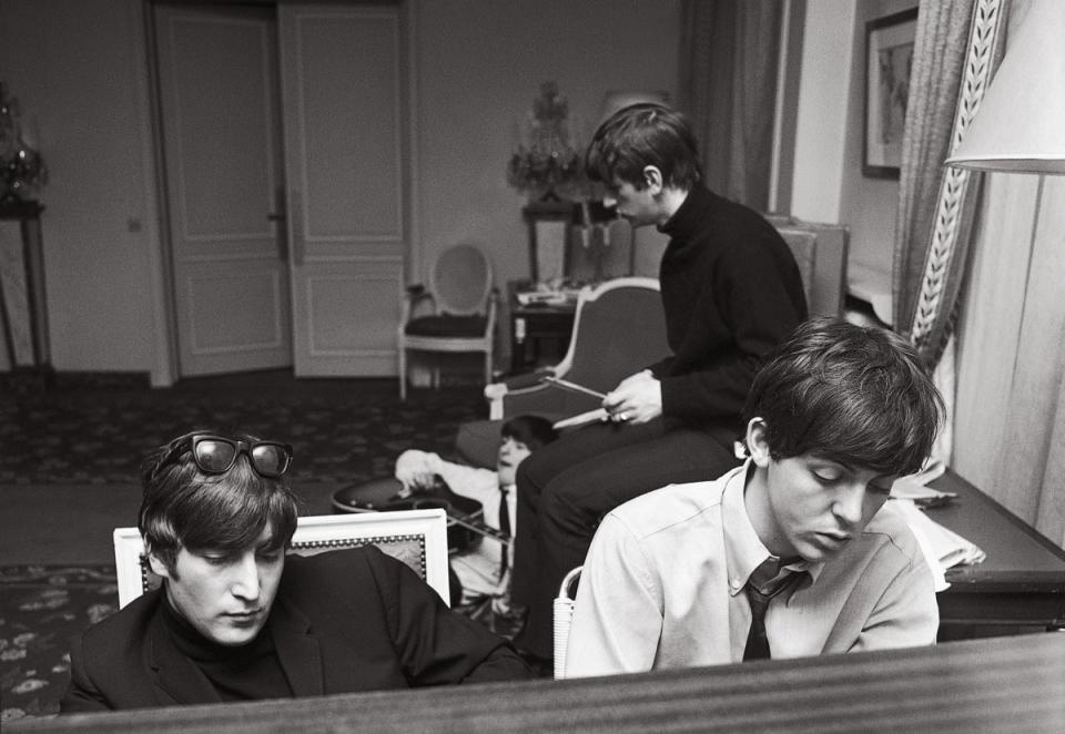 John and Paul deep in thought as they compose at the piano in their suite at the George V Hotel with George and Ringo in the background, January 1964 (Harry Benson)