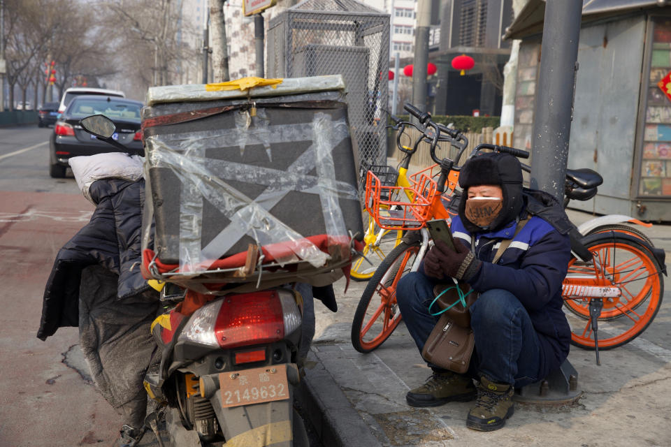 A deliver man uses his phone while waiting on a street of Beijing, China Tuesday, Feb. 11, 2020. China's daily death toll from a new virus topped 100 for the first time and pushed the total past 1,000 dead, authorities said Tuesday after leader Xi Jinping visited a health center to rally public morale amid little sign the contagion is abating. (AP Photo/Ng Han Guan)