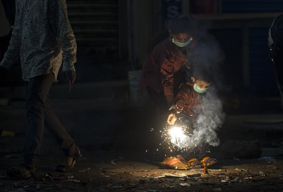 Indians light fire crackers wearing masks to fight pollution as they celebrate Diwali, the festival of lights in Hyderabad, India, Wednesday, Nov. 7, 2018. India's top court recently ruled that only less polluting firecrackers should be manufactured and sold. (AP Photo/Mahesh Kumar A.)