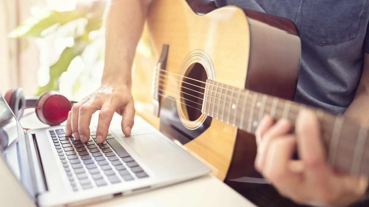  Close up of acoustic guitar playing taking lessons on his laptop. 