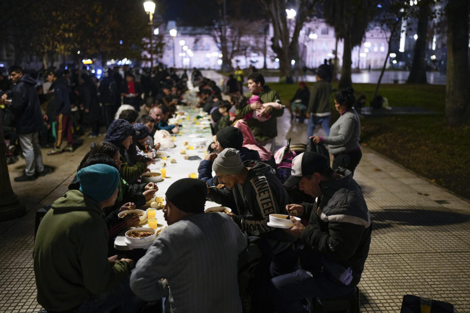 En esta imagen de archivo, un grupo de personas comen los platos que reparte "Red Solidaria" en un comedor benéfico al aire libre que se instala cada noche en la Plaza de Mayo, a unos metros de la sede del gobierno, la Casa Rosada, en Buenos Aires, Argentina, el 6 de junio de 2024. Milei eliminó los controles de precios y recortó drásticamente las subvenciones, lo que disparó los precios en un país que ya tenía una de las tasas de inflación más altas del mundo. (AP Foto/Natacha Pisarenko, archivo)