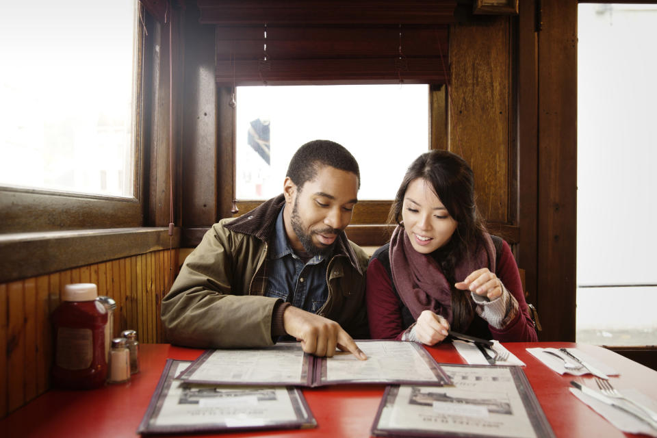 A man and a woman sitting in a diner and looking at a menu