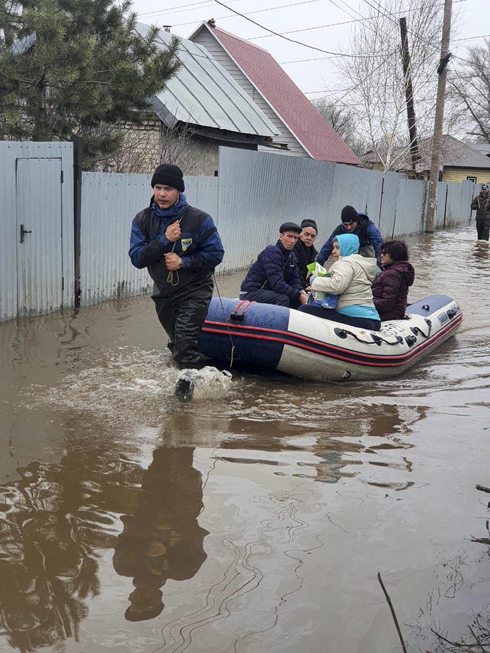 In this photo released by the Administration of the city of Orenburg telegram channel on Saturday, April 6, 2024, an emergency worker pulls a boat evacuating a group of local residents after a part of a dam burst causing flooding, in Orsk, Russia. (Administration of the city of Orenburg Telegram Channel via AP)