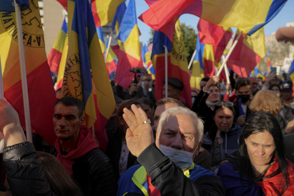 A man shields his face from the sun as people wave flags during an anti-government protest organised by the far-right Alliance for the Unity of Romanians or AUR, in Bucharest, Romania, Saturday, Oct. 2, 2021. Thousands took to the streets calling for the governments resignation, as Romania reported 12.590 new COVID-19 infections in the past 24 hour interval, the highest ever daily number since the start of the pandemic. (AP Photo/Vadim Ghirda)