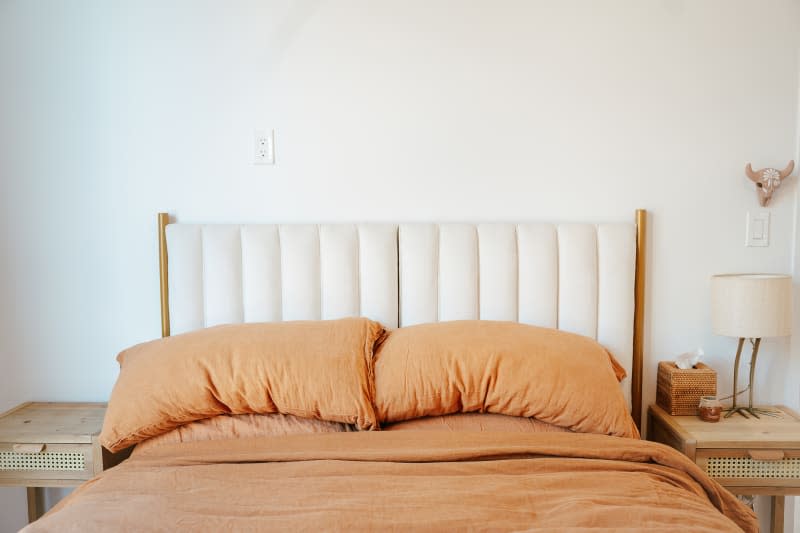 White upholstered headboard in bedroom with neatly made bed with burnt orange linens.