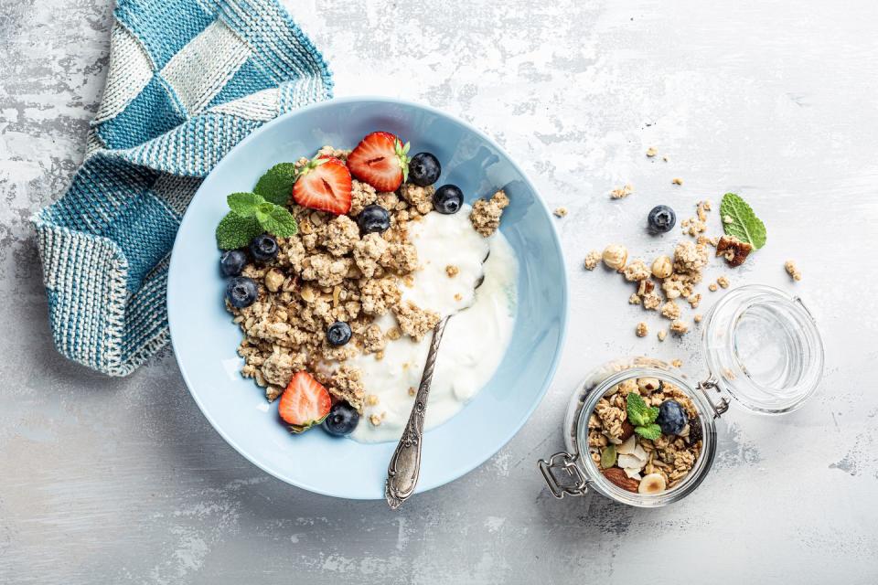 overhead schoot of granola with nuts mix, yogurt, fresh berries and honey on blue plate voor healthy breakfast, top view, copy space