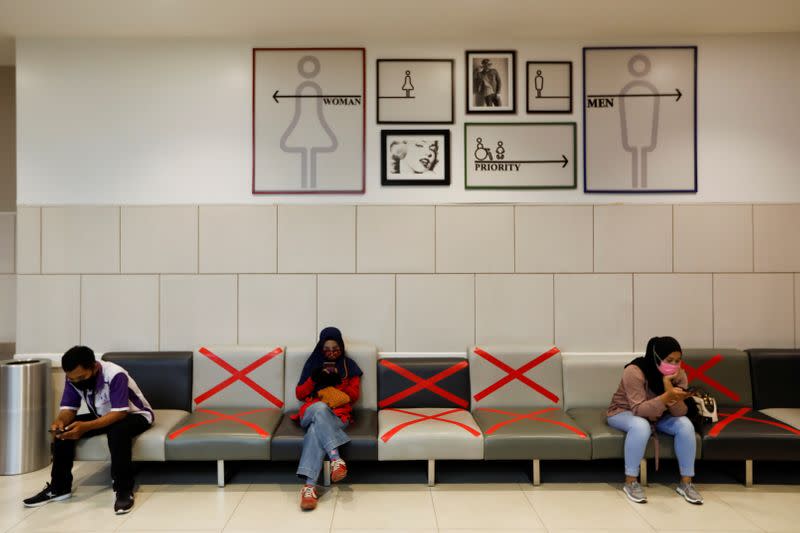 People wearing face masks use their phones and while sitting inside a shopping mall in Tangerang, on the outskirts of Jakarta