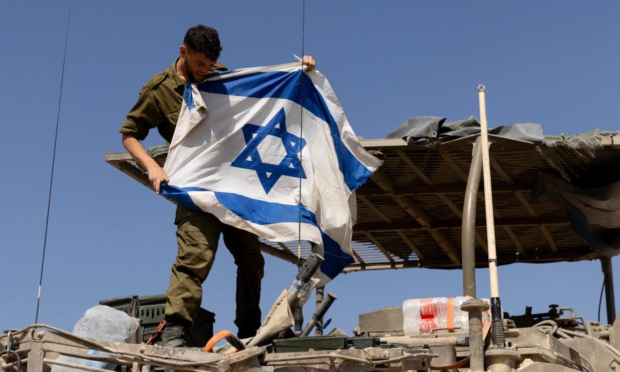 <span>A soldier hangs an Israeli flag on an armoured personnel carrier near the border with Gaza.</span><span>Photograph: Amir Levy/Getty Images</span>