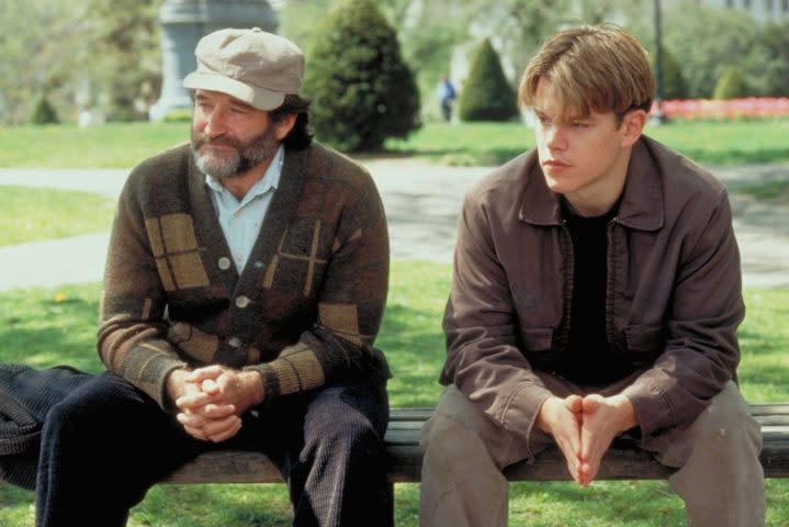 Robin Williams and Matt Damon sit next to each other on a bench.