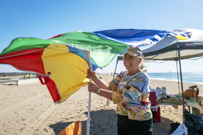 HUNTINGTON BEACH, CA - NOVEMBER 25: Sue West of Costa Mesa holds on to her unbrella as the winds kick up at Bolsa Chica State Beach at on Thursday, Nov. 25, 2021 in Huntington Beach, CA. West is setting up their site on the beach as they prepare for Thanksgiving dinner. Later in the day the winds calmed in time for dinner. (Francine Orr / Los Angeles Times)
