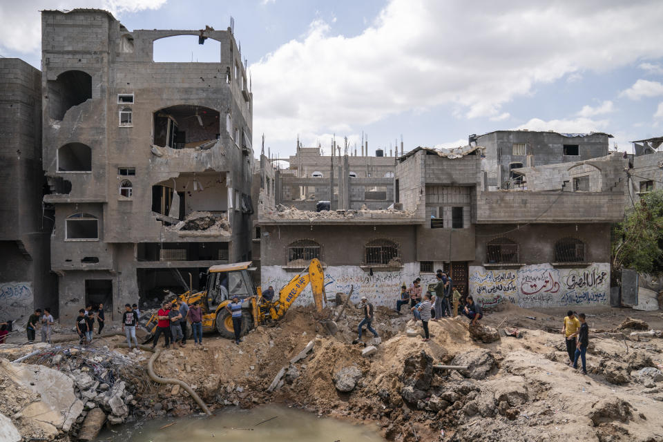 Neighbors gather to watch the cleanup of a crater full of water and sewage after the home of Ramez al-Masri was destroyed by an air-strike prior to a cease-fire reached after an 11-day war between Gaza's Hamas rulers and Israel, Sunday, May 23, 2021, in Beit Hanoun, the northern Gaza Strip. (AP Photo/John Minchillo)