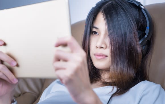 An Asian girl watches a video on a tablet.