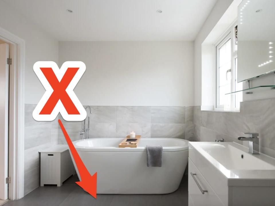red x and arrow pointing at gray flooring in a minimal bathroom with a tub