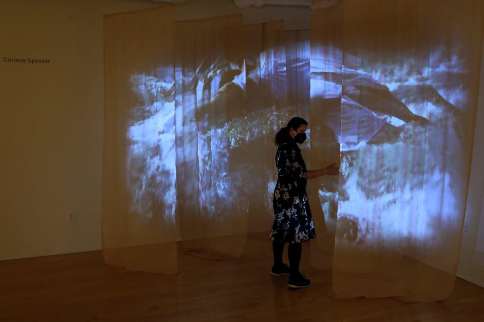 Co-curator Viera Levitt feels the sheets of linen hanging from the wall where a video is being projected upon.  This piece by Corinne Spencer is one of many included in the Sheltered show being shown in the gallery of the UMass Dartmouth CVPA.