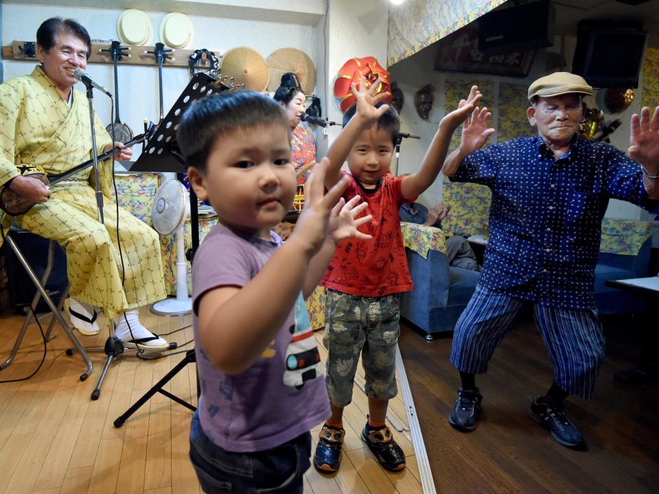 In this photo taken on June 20, 2016, and elderly man (R) and children dance to the sounds of the sanshin - a banjo-like instrument - played by Tatsuo Chinen (L) at a pub in Naha, Okinawa prefecture.